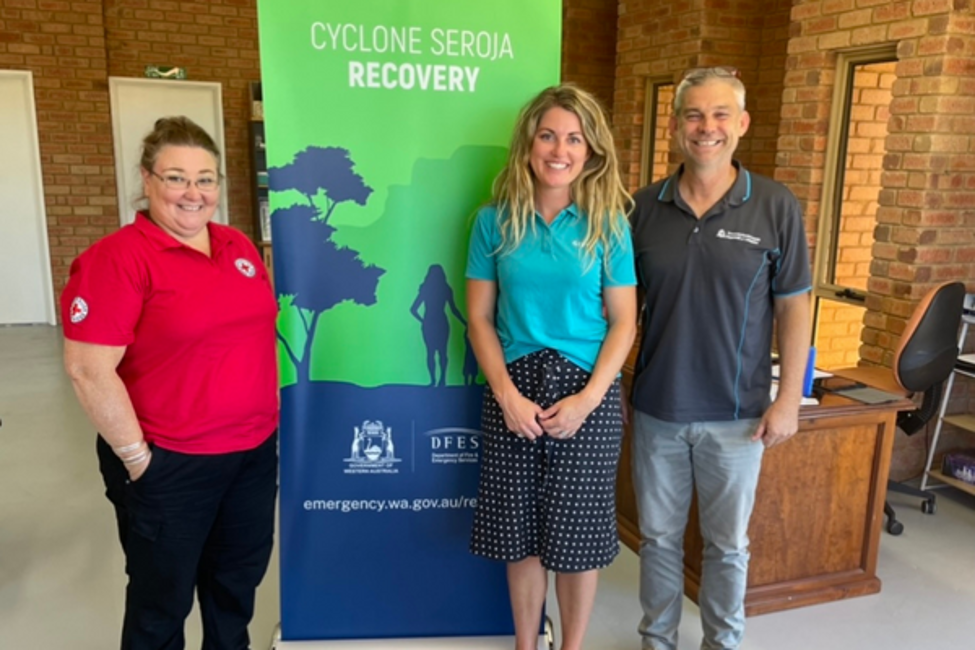 A lady (GIVIT Engagement Officer Sarah Visser), standing with another lady with a Red Cross shirt, and a man with a WA State Government shirt on, in front of a WA Government pull up banner